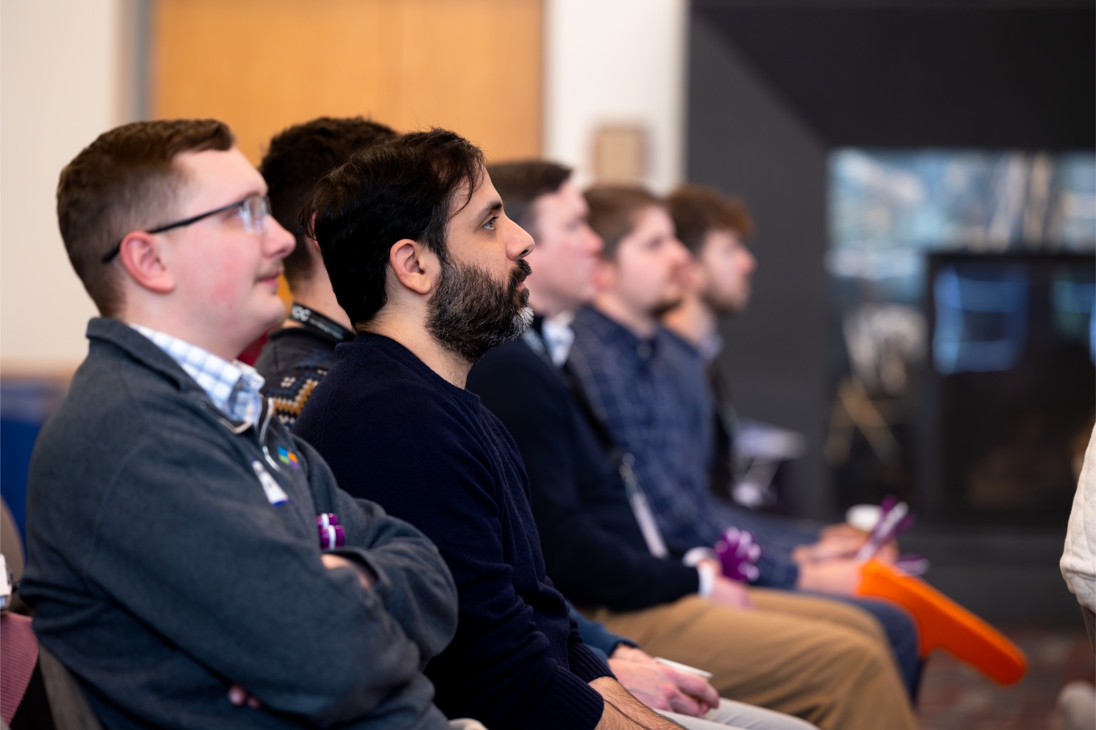 A group of men attentively listening in a seminar room setting. A group of men attentively listening in a seminar room setting.