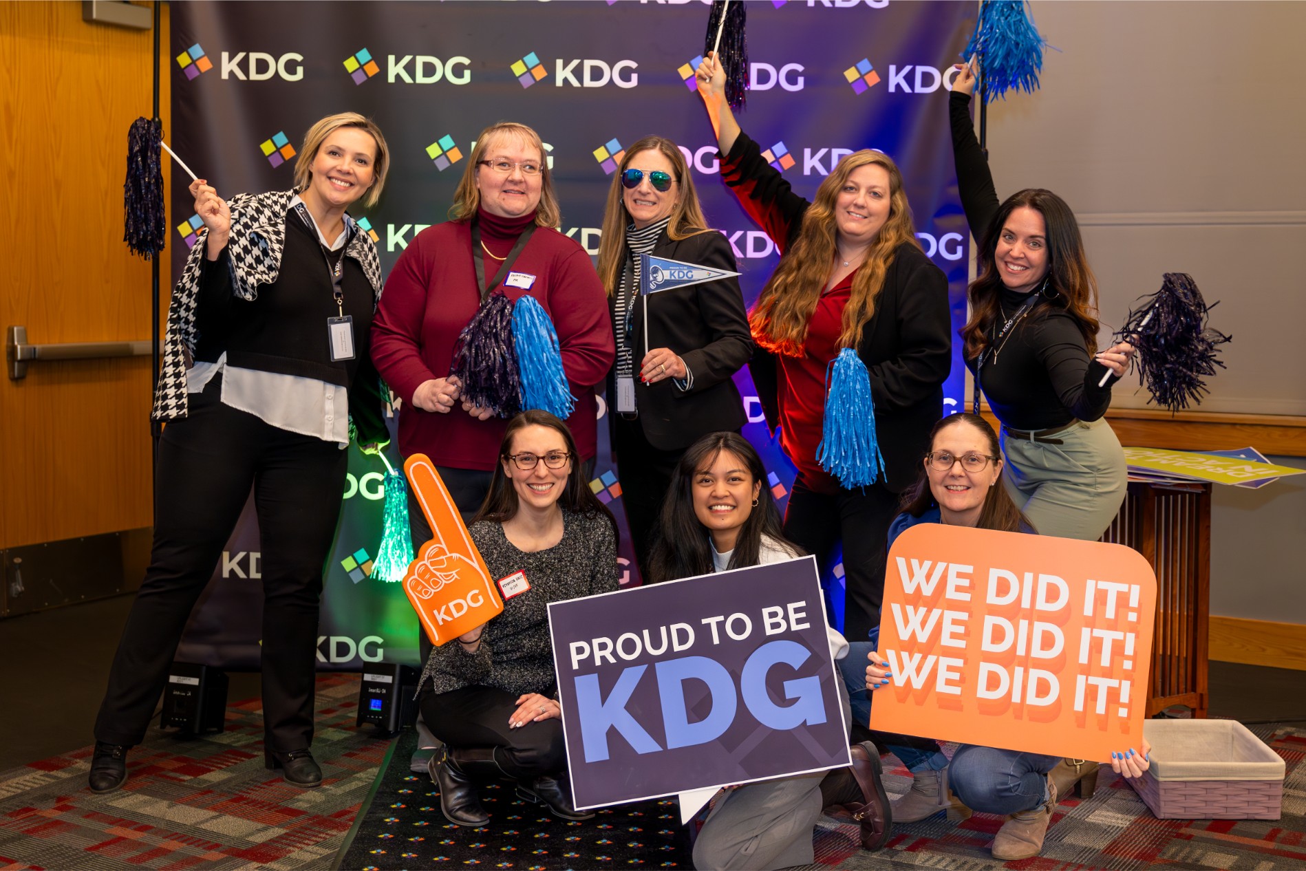 A group of people pose with KDG signs and pom-poms at an indoor event. A group of people pose with KDG signs and pom-poms at an indoor event.