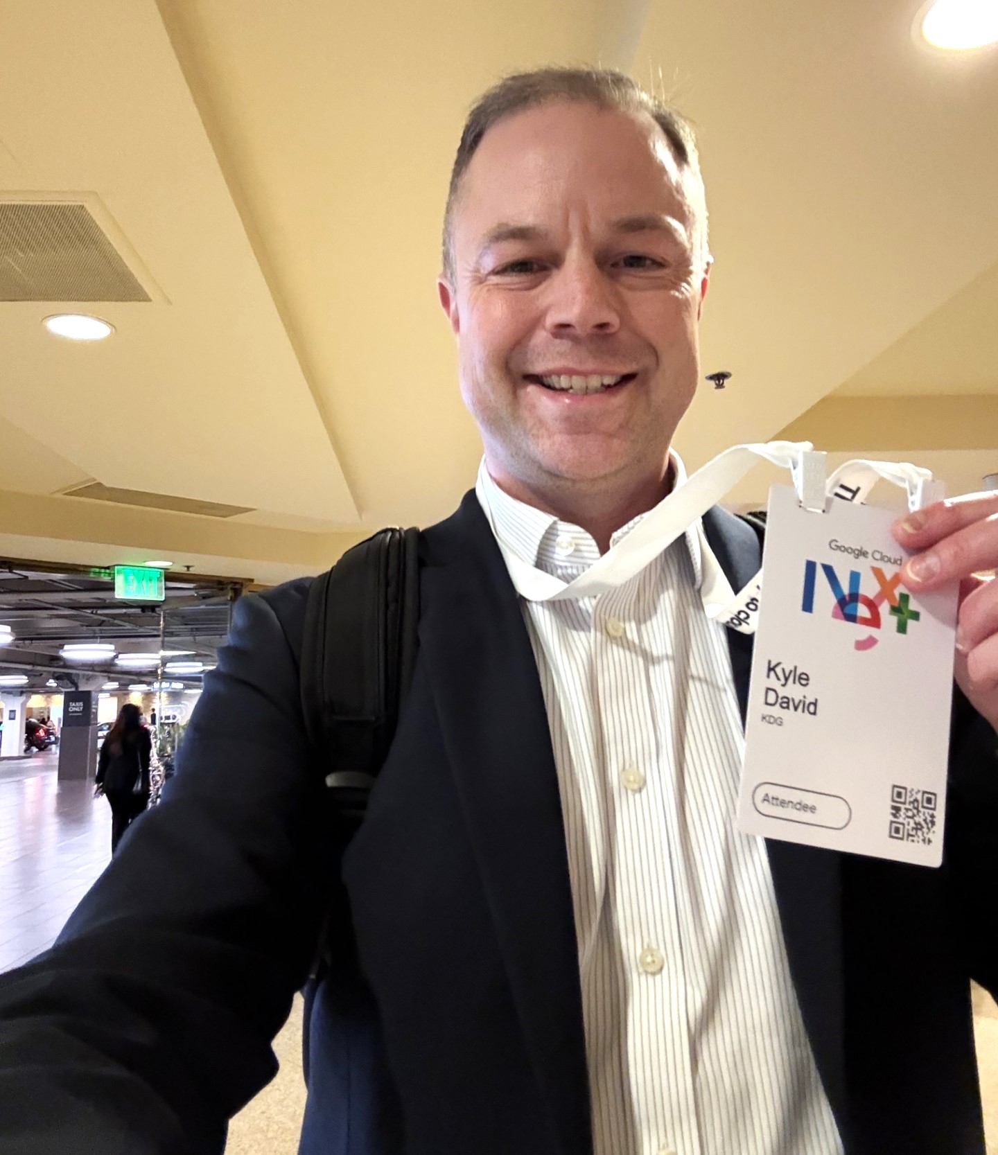 Man in a suit holding a "Kyle David" conference badge at Google Cloud Next 2025, standing in a hallway with a backpack.