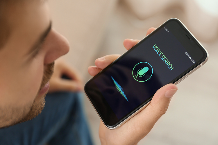 A person holds a smart phone in their hand with the icon for voice search showing on screen while they speak.
