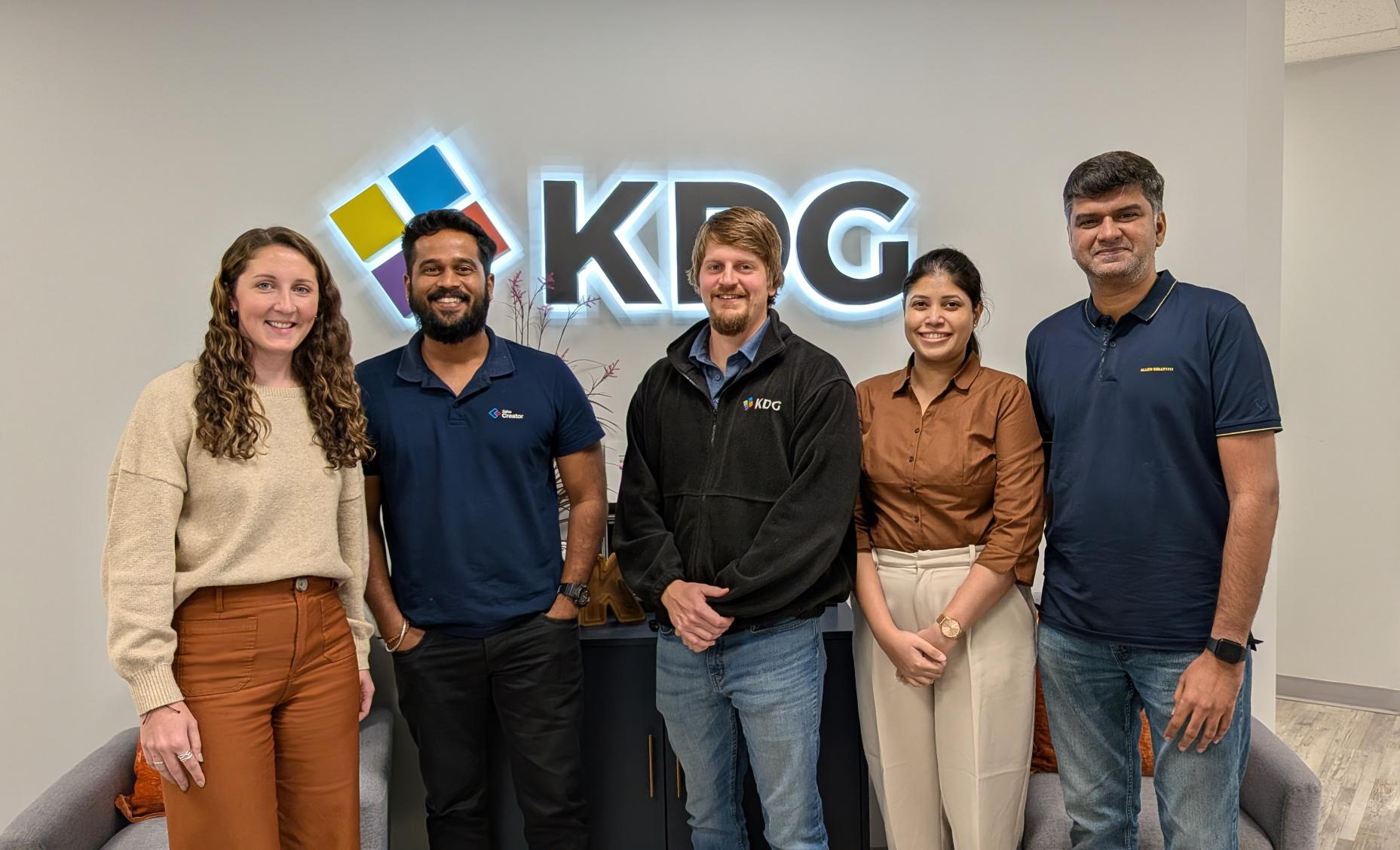 Five people stand in front of a wall with a KDG logo, posing for a group photo in a modern office setting—celebrating their new strategic plan for 2026 Zoho Creator marketing efforts in partnership with KDG.