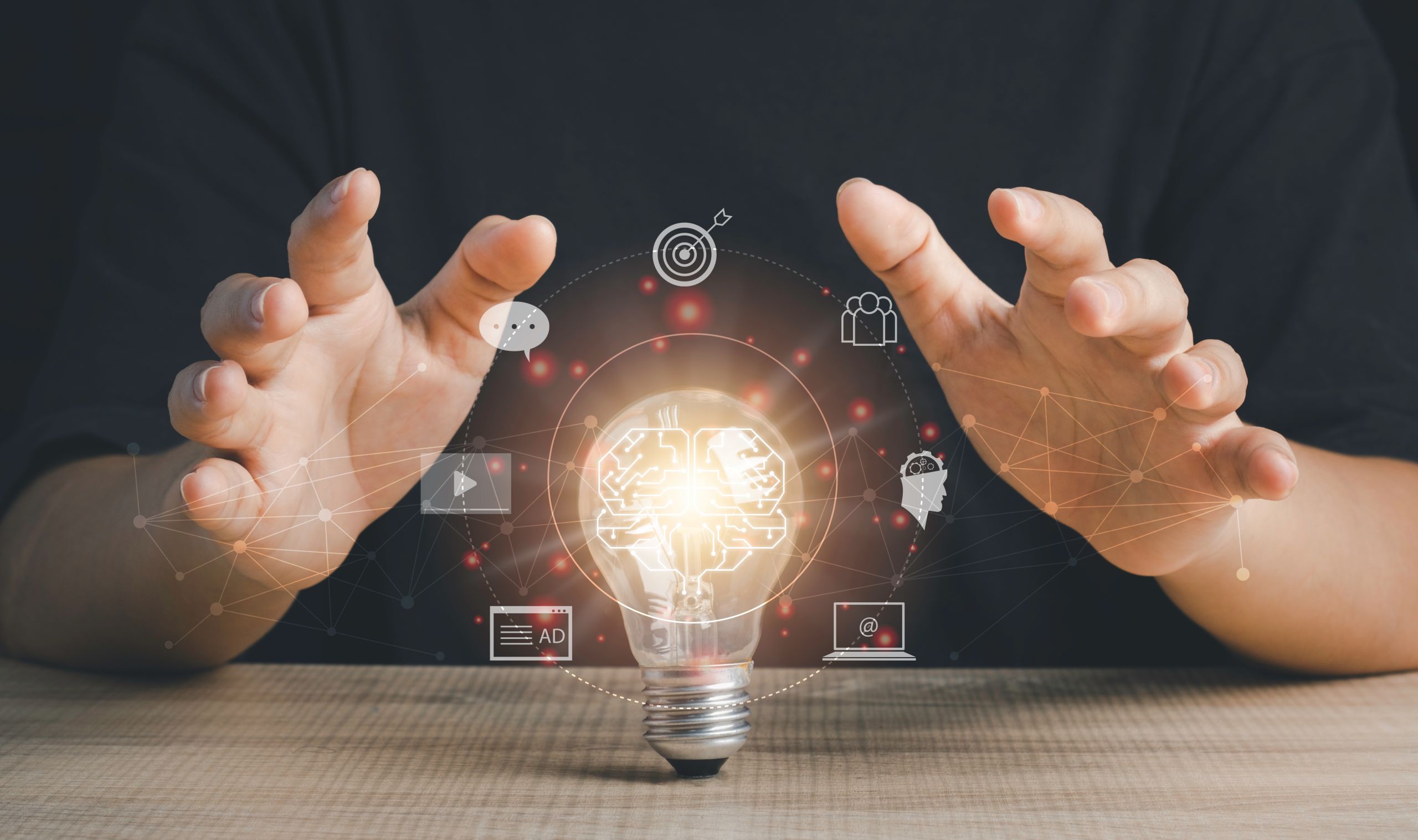 A person holds their hands around a glowing light bulb with a brain graphic, surrounded by digital business, technology, and Social Media icons.