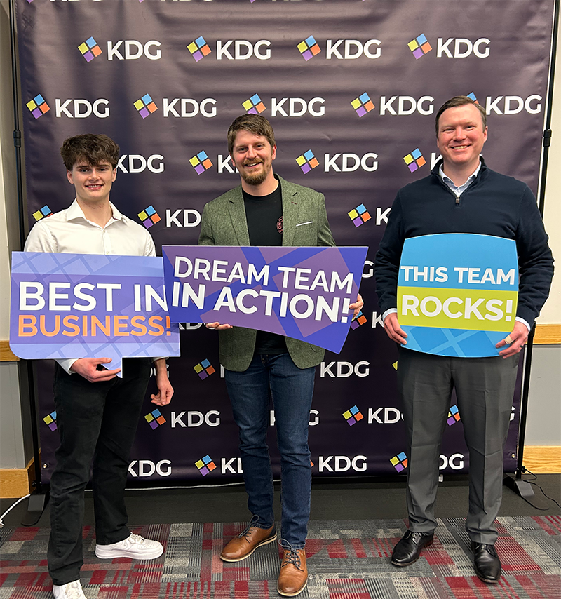 Three men stand in front of a KDG backdrop holding signs that read “Best in Business!”, “Dream Team in Action!”, and “This Team Rocks!”—celebrating their success in Zoho Development. Three men stand in front of a KDG backdrop holding signs that read "Best in Business!", "Dream Team in Action!", and "This Team Rocks!"—celebrating their success in Zoho Development.